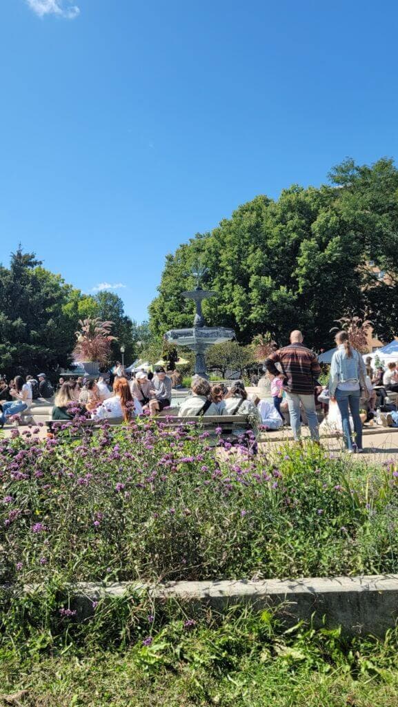 Wicker Park fountain with crowds enjoying the market and purple flowers in foreground